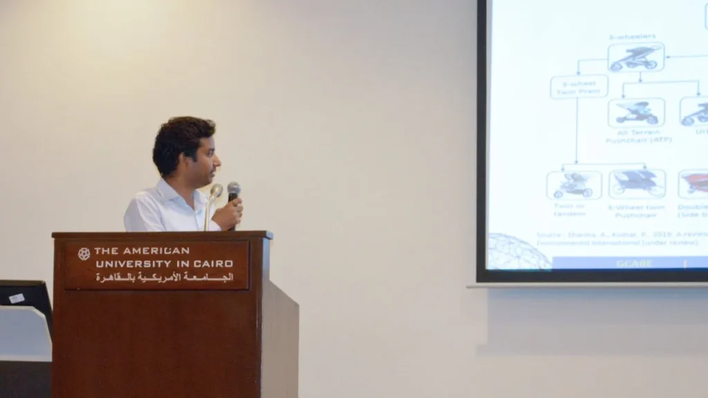 A presenter speaking at an American University in Cairo lectern beside a projected diagram.