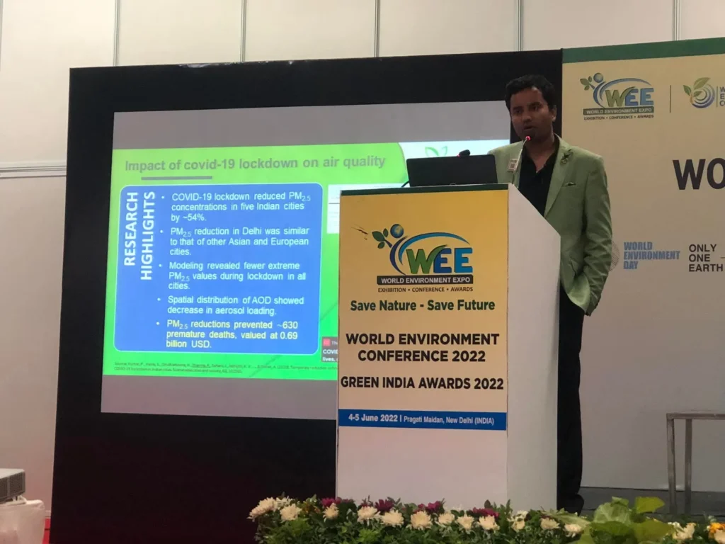 A presenter speaking at the World Environment Conference lectern beside an air quality slide.