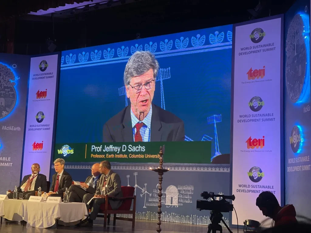 A remote speaker on screen above the seated summit panel.